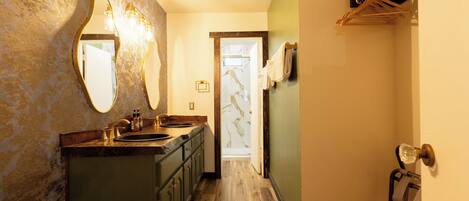 A narrow hallway with a wooden floor, a sink with a marble countertop, and a mirror with wall-mounted lights.