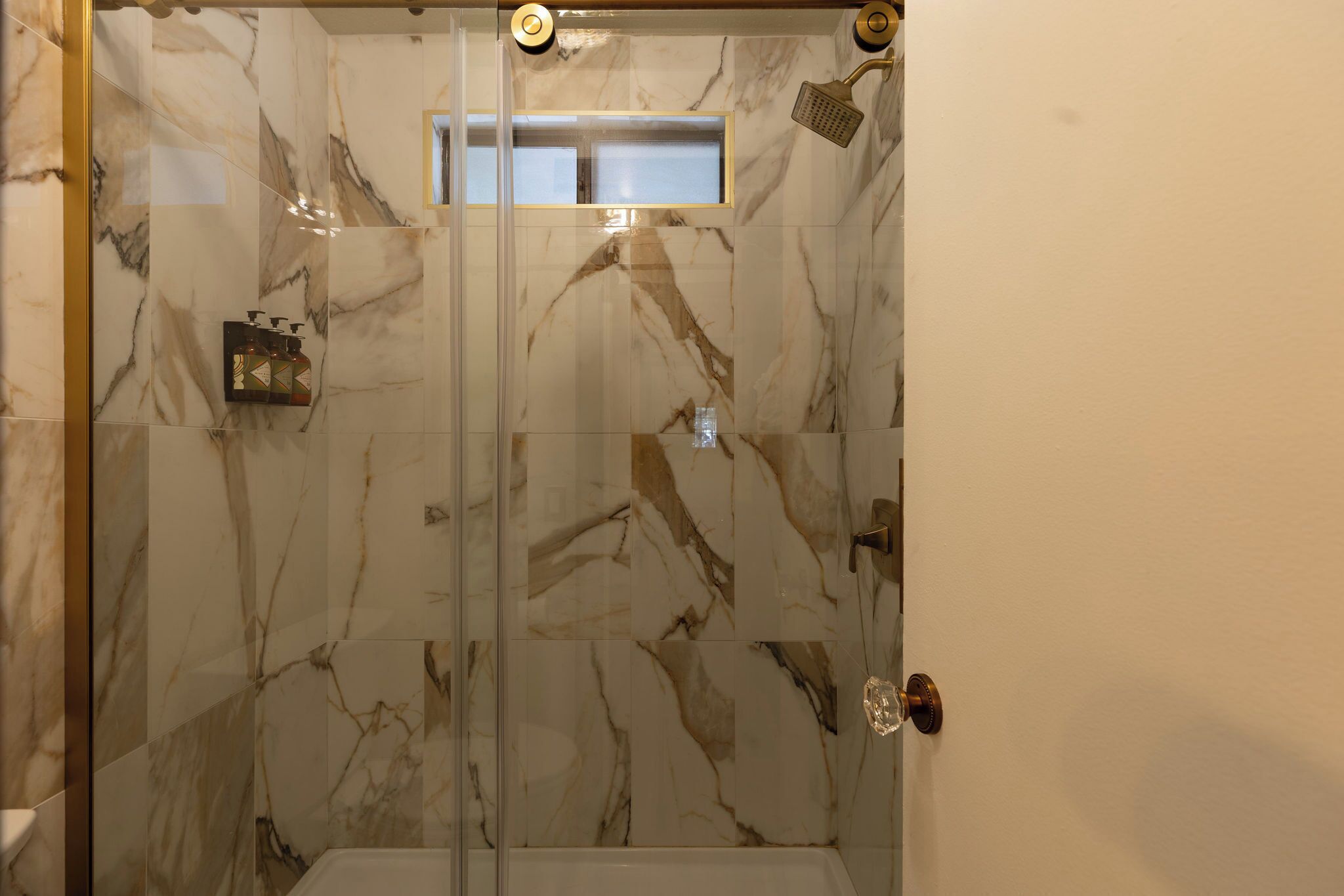 A glass-enclosed shower with marble walls and a visible showerhead.