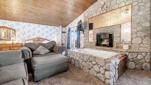 A cozy living room with a stone fireplace, a large tub, and a wooden ceiling.