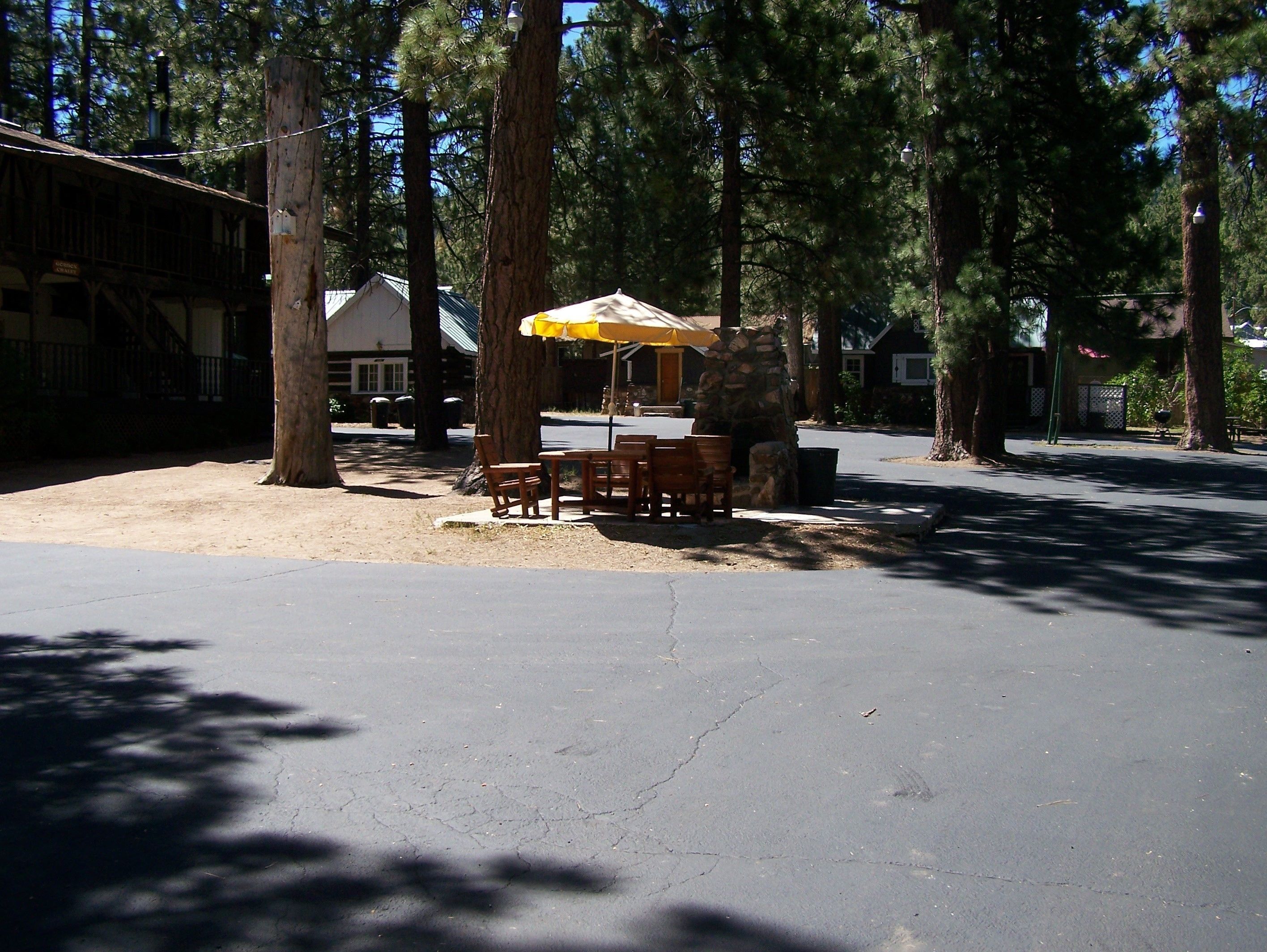A picnic table with chairs and a yellow umbrella in a wooded area.