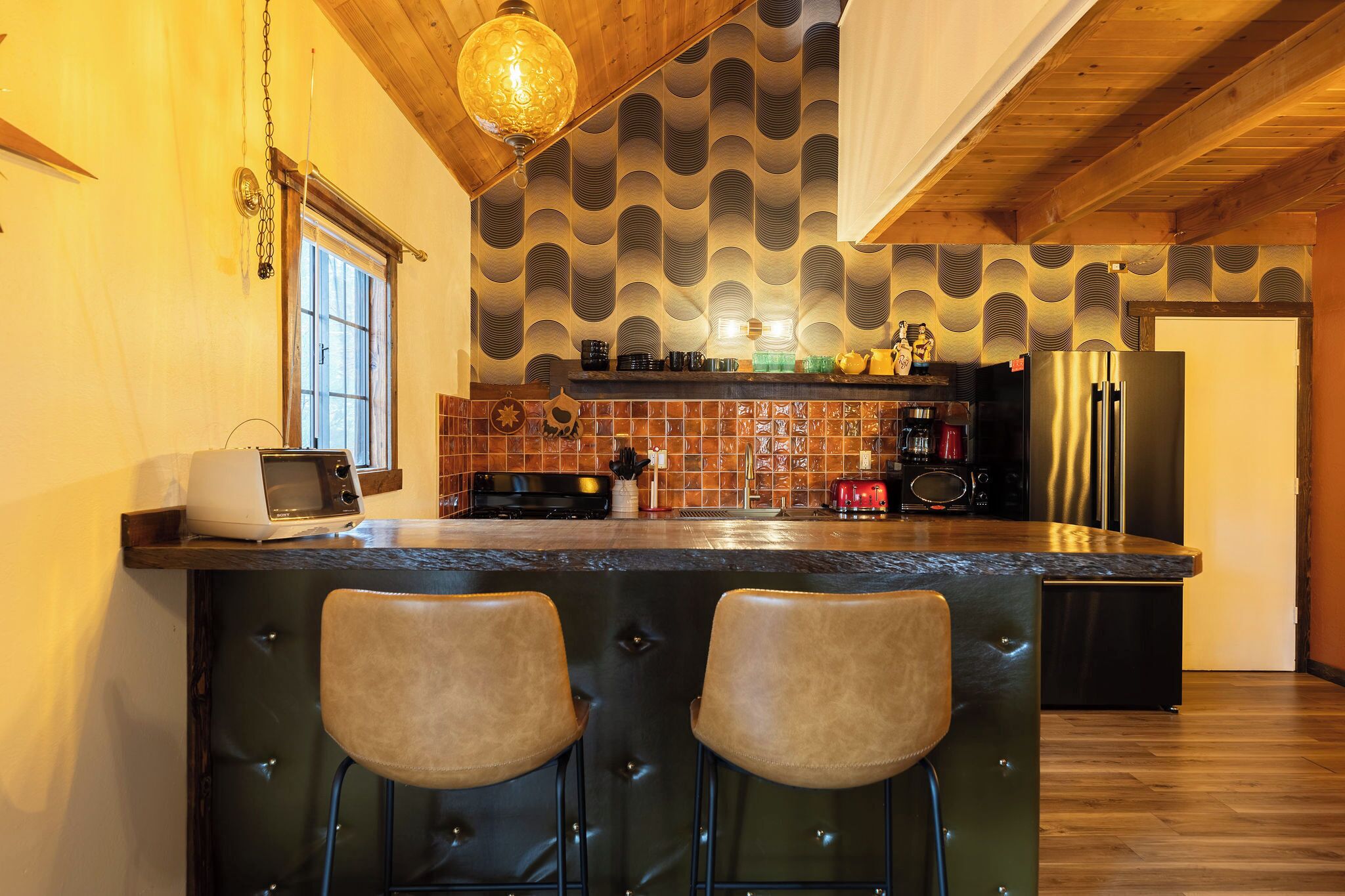 A kitchen with a central island, bar stools, a microwave, a toaster, and a refrigerator.