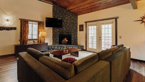 A cozy living room with a stone fireplace, wooden ceiling, and a large window.