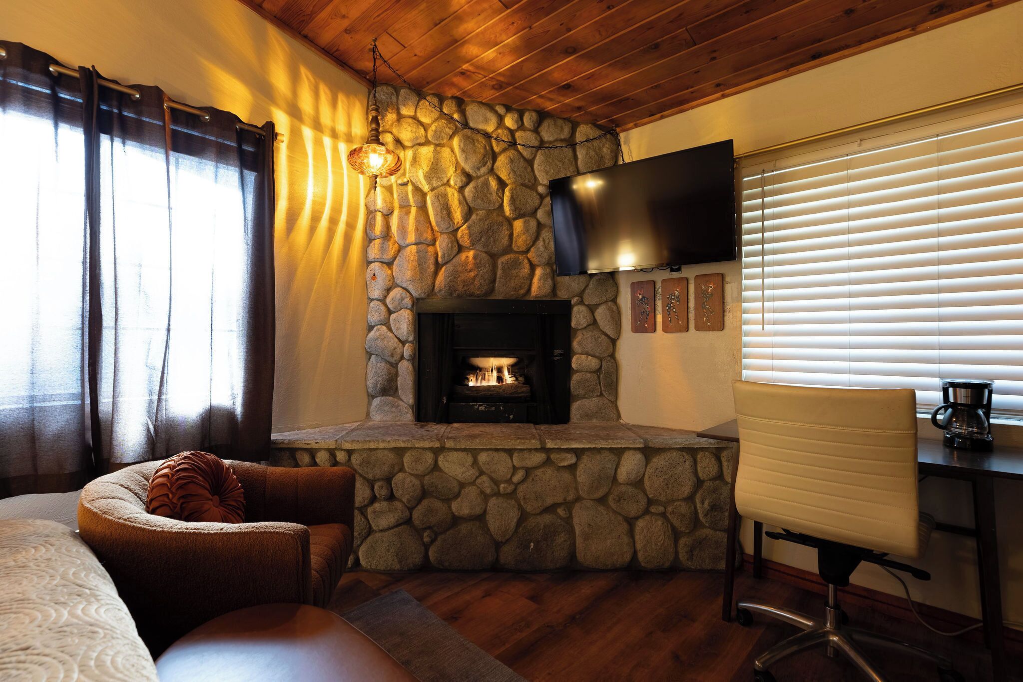 A cozy room with a stone fireplace, a flat-screen TV mounted above it, and a comfortable seating area with a cushioned chair and ottoman.