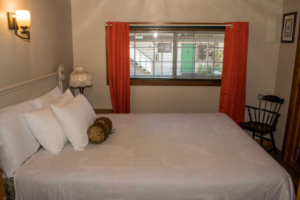 A neatly made bed with white linens, a bedside lamp, and a chair to the right.