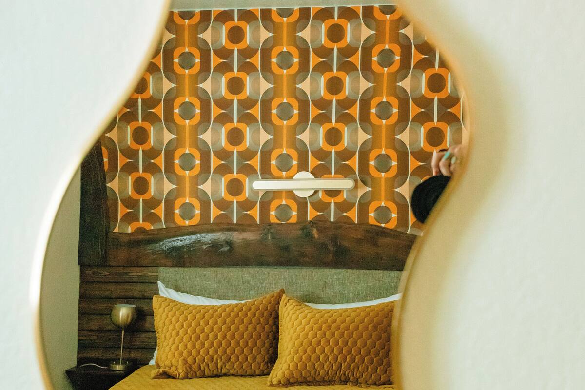 A room with a bed, a wooden headboard, and a patterned wall.