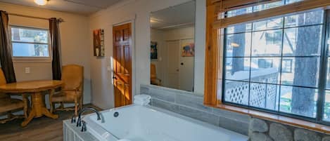 Un baño con una bañera grande, una mesa de madera con sillas y una pared de piedra.