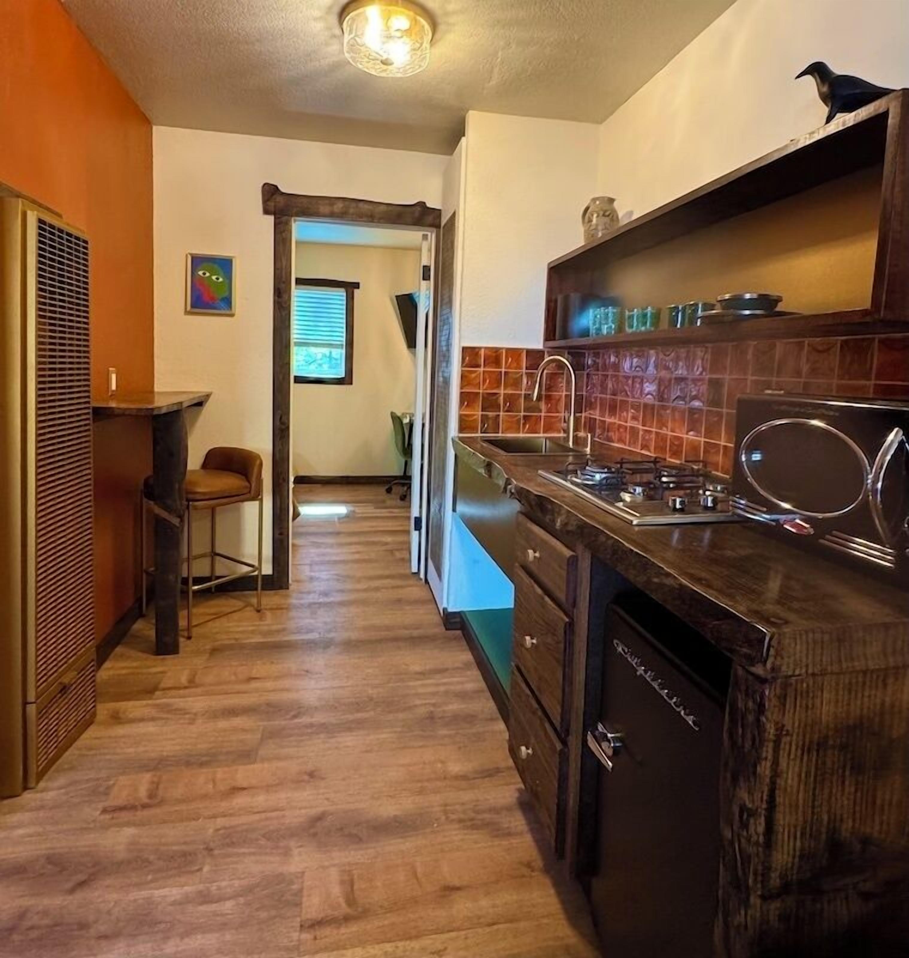 A kitchen with wooden cabinets, a sink, and a stove. There is a chair and a window with blinds in the background.