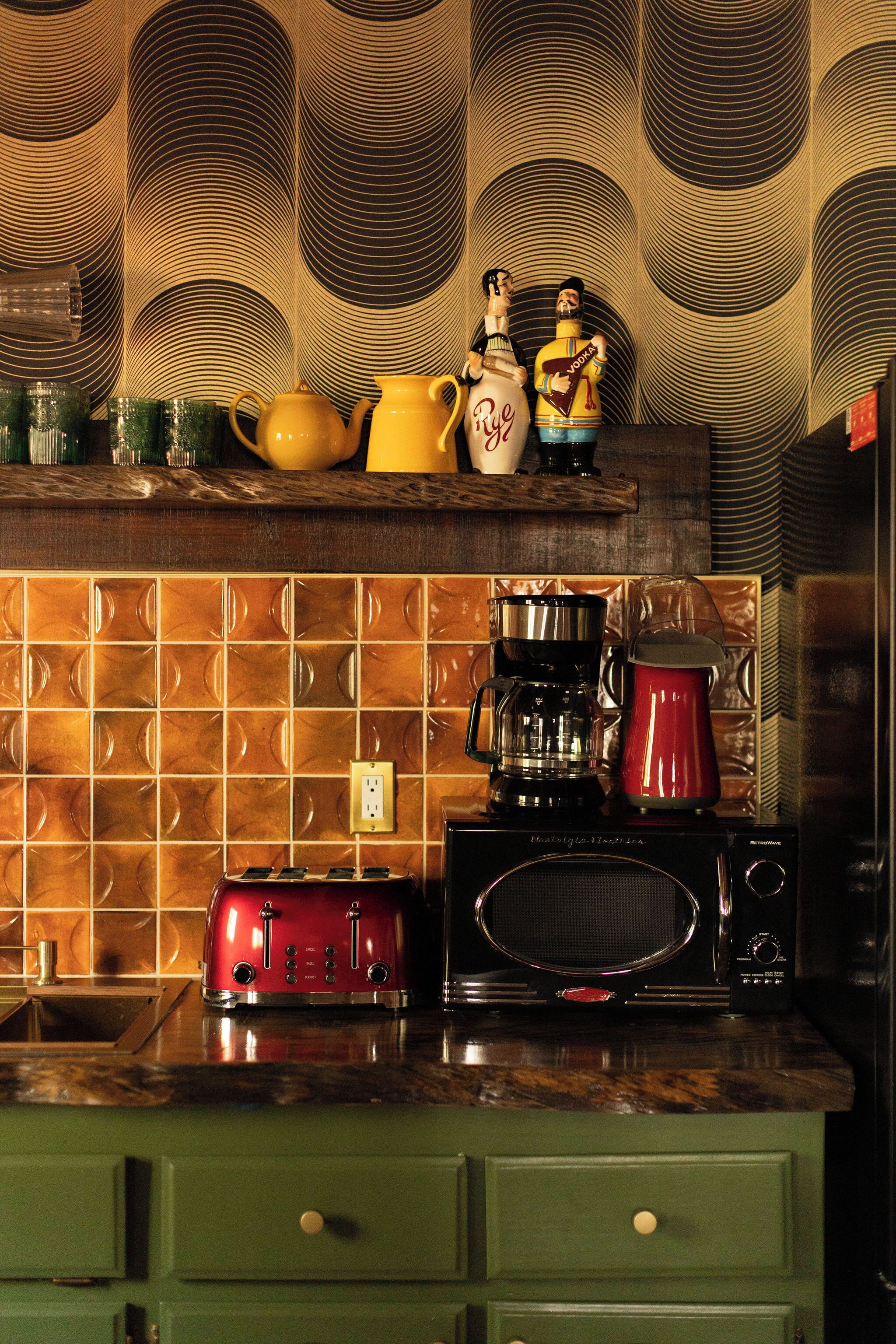 A kitchen with a patterned backsplash, a coffee maker, a red toaster, and a microwave.