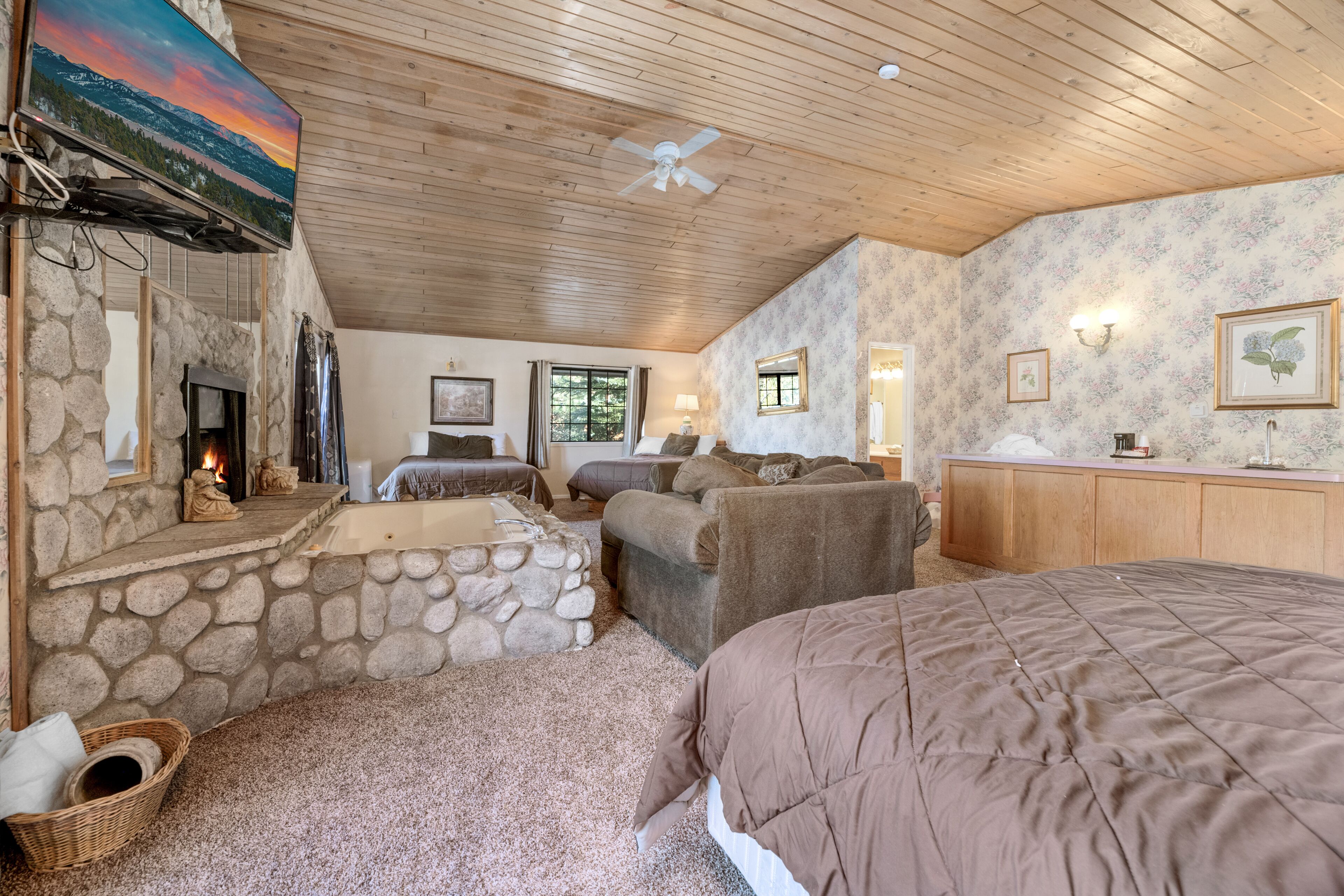 A cozy room with a stone fireplace, a large bed, a sofa, and a television mounted on the wall.