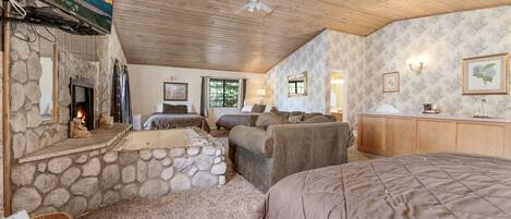 A cozy room with a stone fireplace, a large bed, a sofa, and a television mounted on the wall.