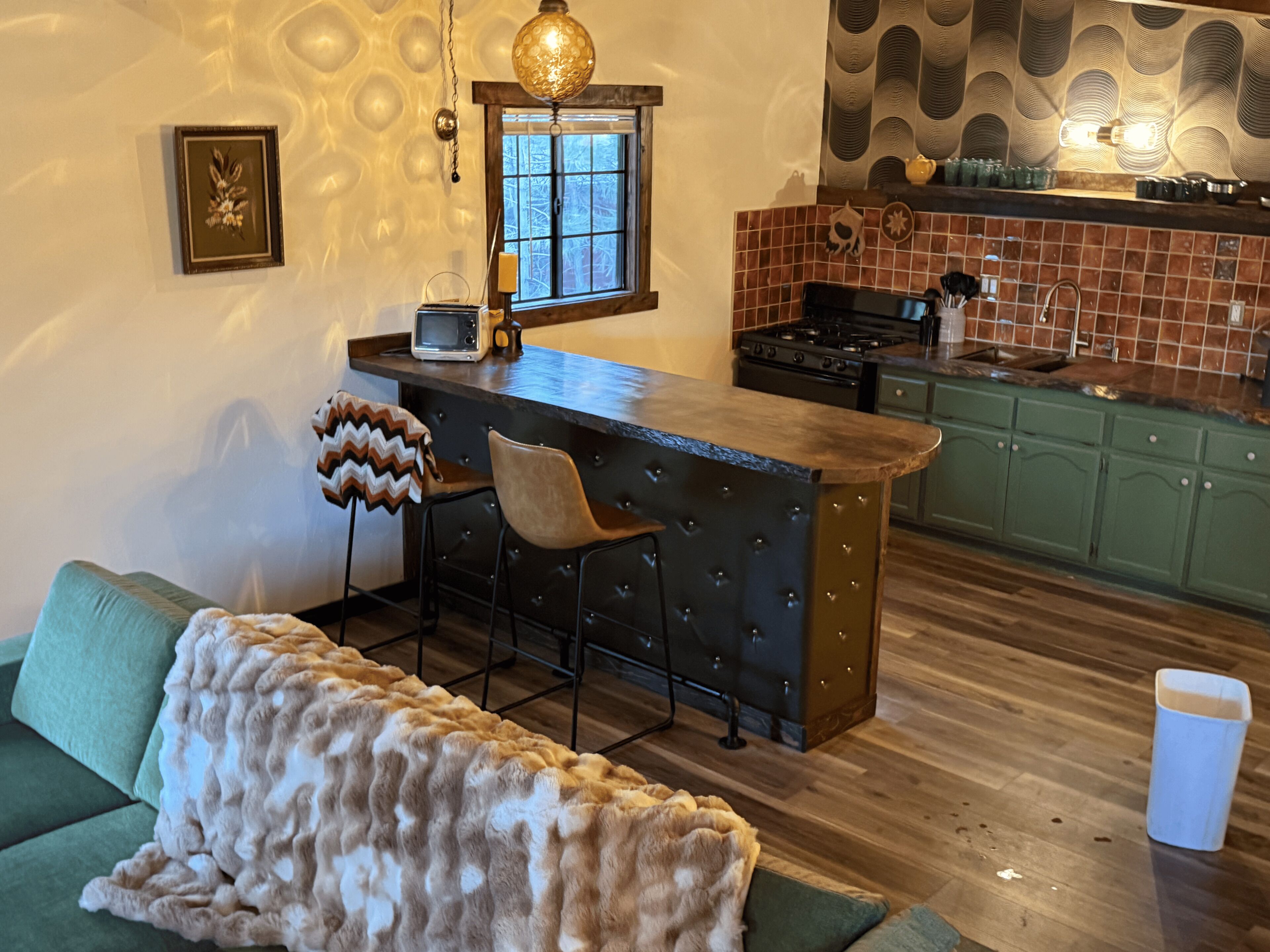 Una cocina acogedora con barra, armarios verdes y salpicadero con diseño.
