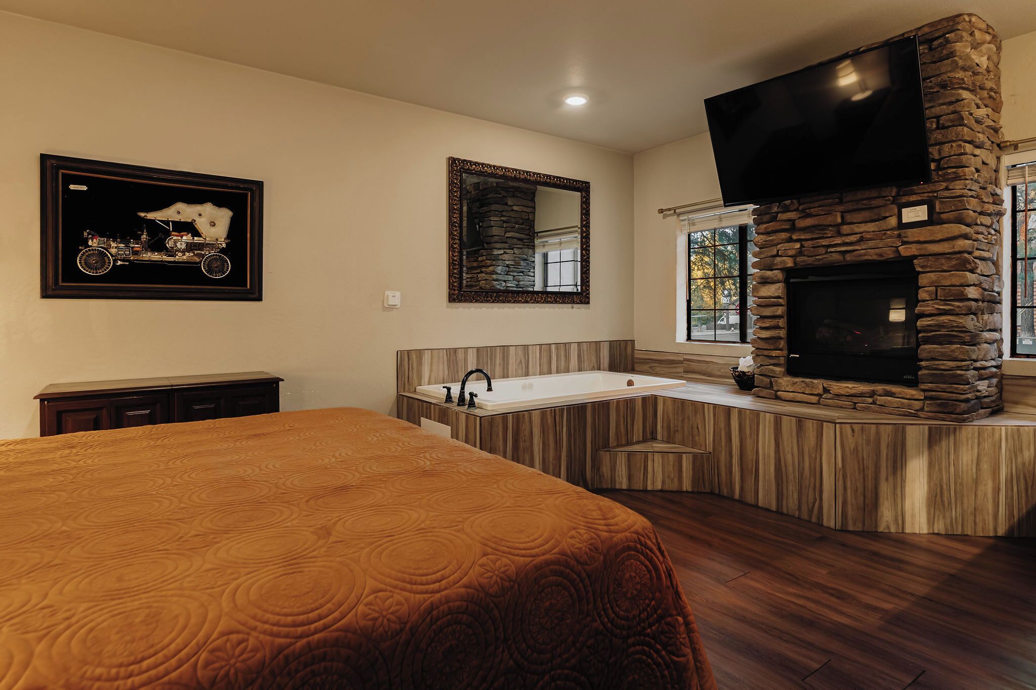 A bedroom with a large bed, a bathroom with a stone fireplace, and a mounted television.