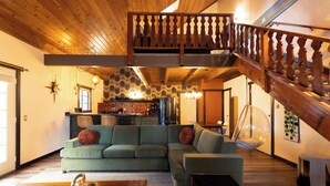 A spacious living area with a green sofa, wooden ceiling, and a wooden staircase.