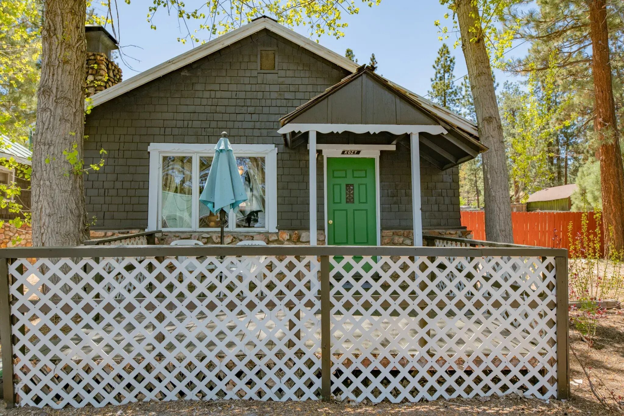 A small wooden cabin with a green door and a white lattice fence in front.
