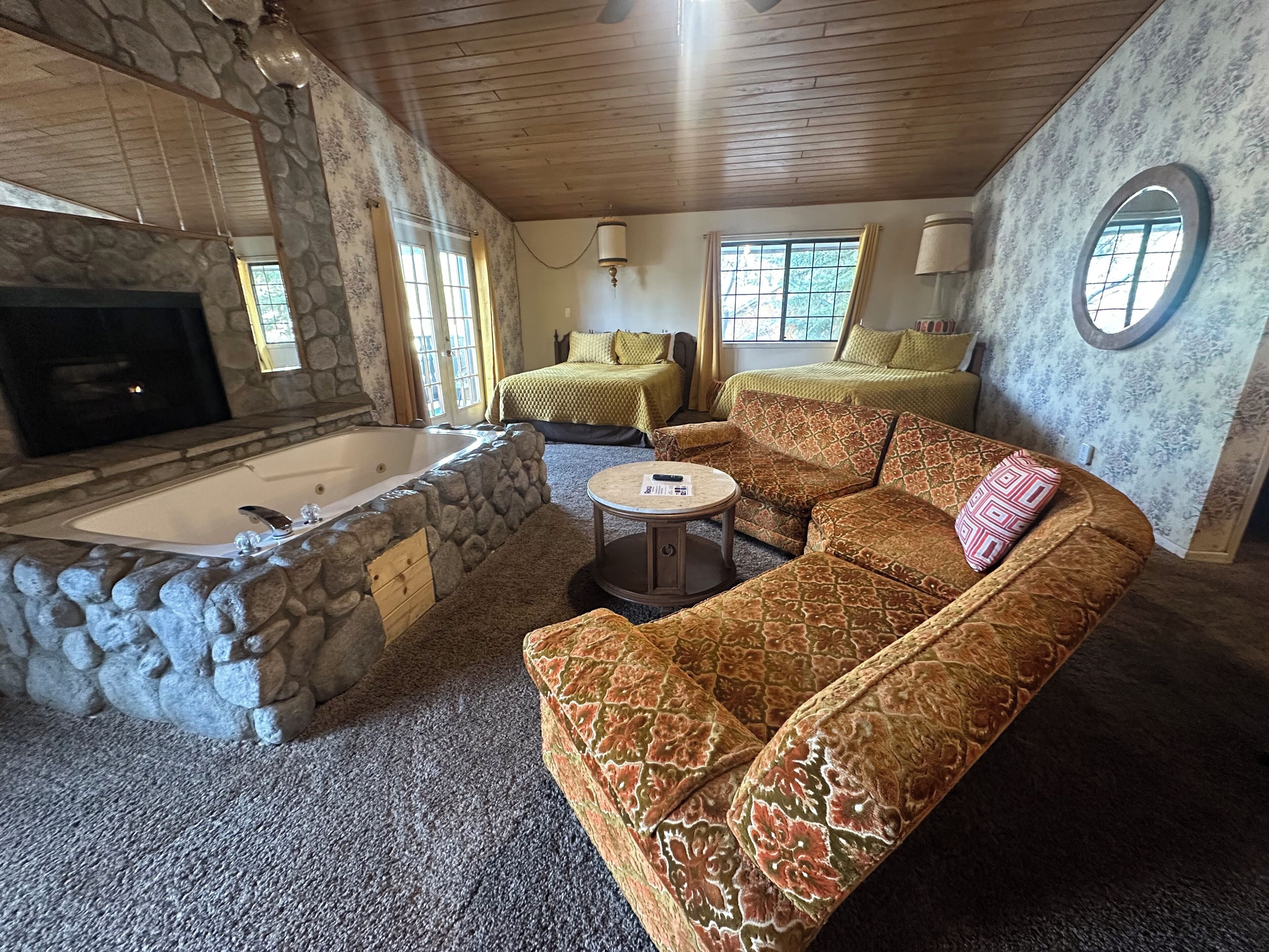 Una habitación acogedora con chimenea de piedra, un sofá grande, una mesita de centro redonda y una bañera.