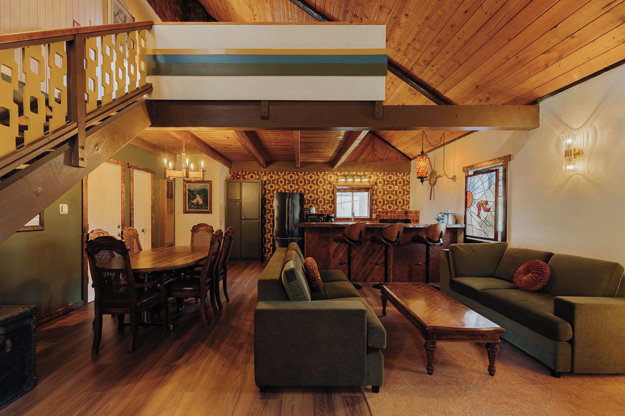 A spacious living area with a wooden staircase, a dining table with chairs, a sofa, and a coffee table.