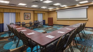 Un salón de conferencias con una larga mesa, sillas, una pantalla de proyector y piso alfombrado.