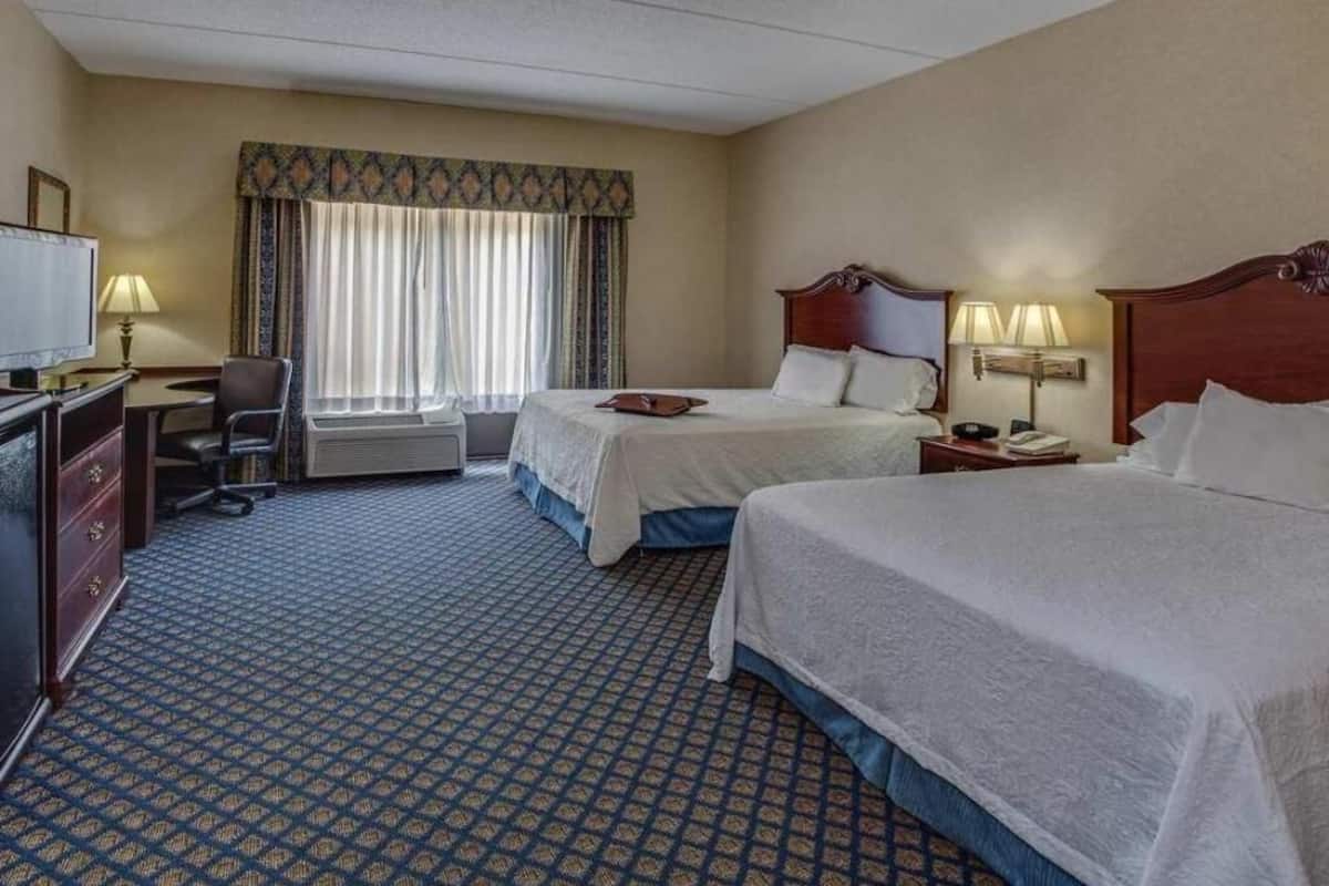 A hotel room with two beds, a desk with a chair, a television, and a window with curtains.