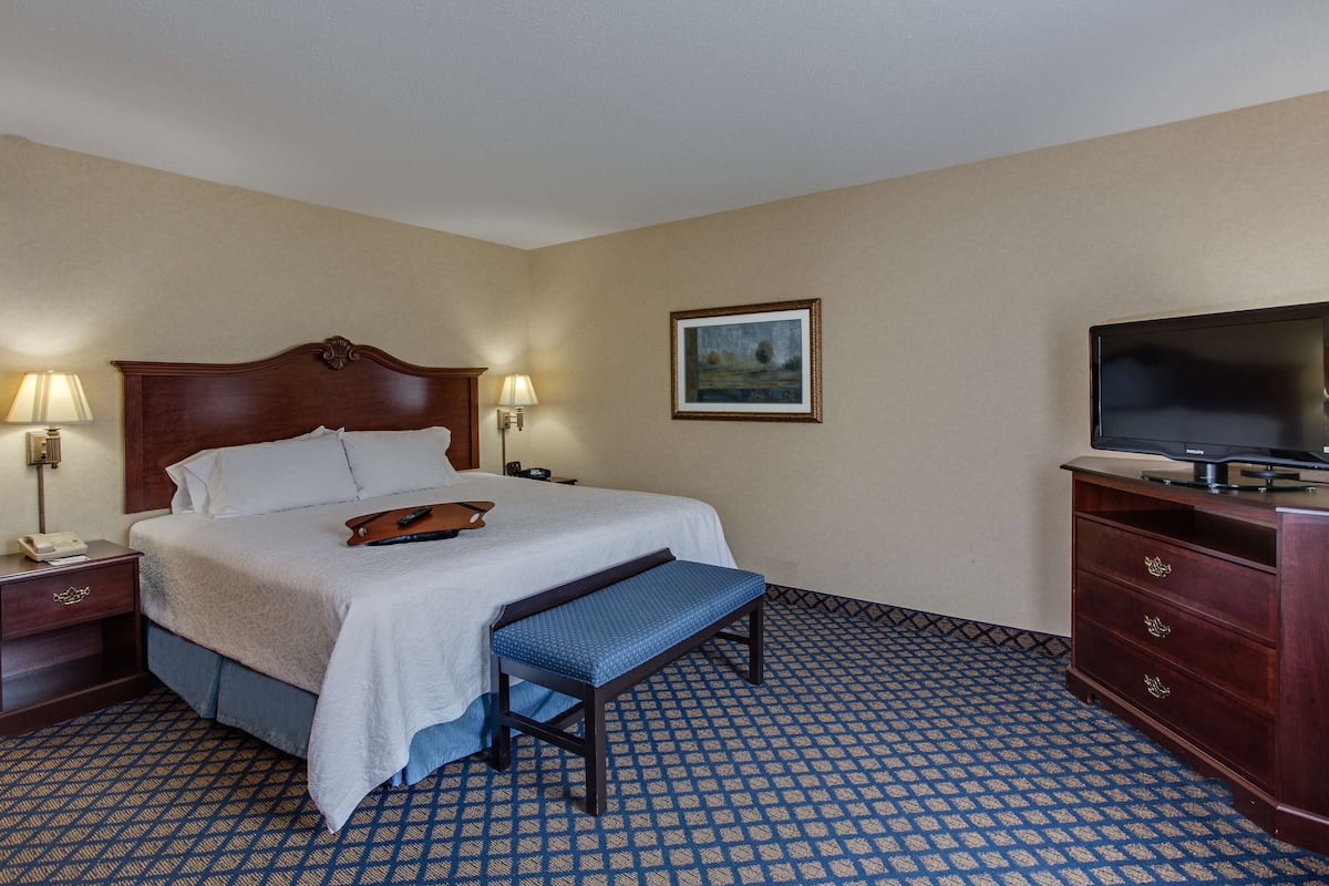 A hotel room with a bed, bedside lamps, a bench, a dresser, a television, and a framed picture on the wall.