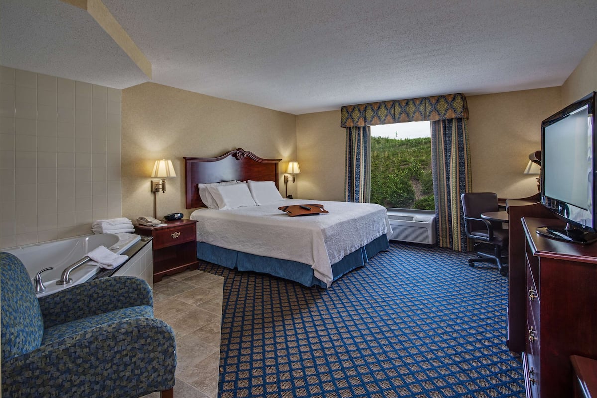 A hotel room with a large bed, a desk, a chair, a television, and a bathroom with a bathtub and sink.