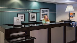 Un mostrador de recepción de hotel con un cartel que dice 'Welcome to Clearwater', fotografías enmarcadas en la pared y un cartel de 'Hilton Honors'.
