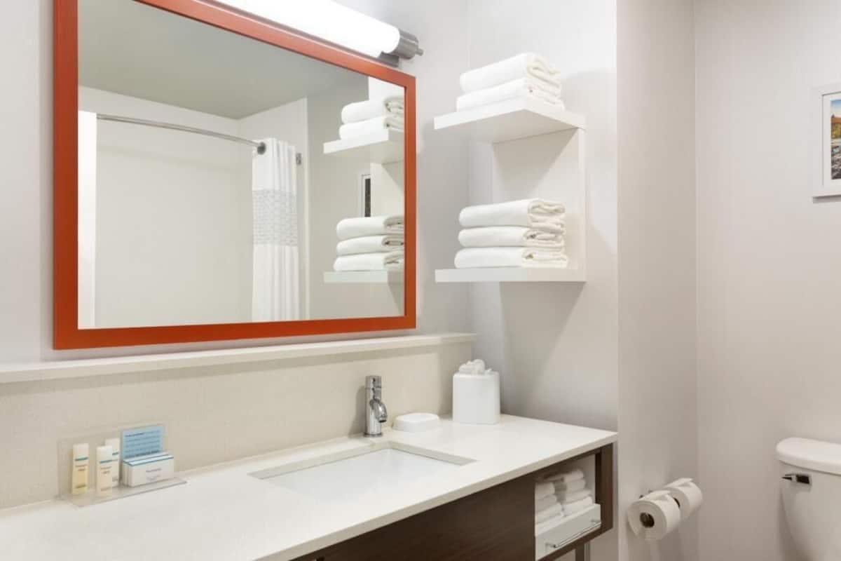 A bathroom with a large mirror, white sink, towel racks, and a toilet.