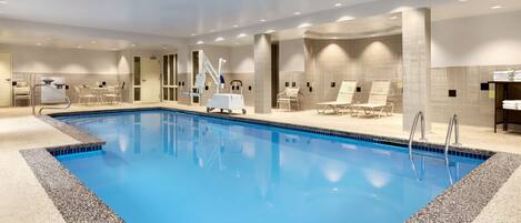 An indoor swimming pool with clear blue water, surrounded by lounge chairs and a changing area.