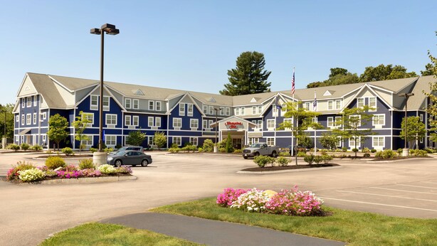 A multi-story hotel with a blue and white exterior, a parking lot, and a well-maintained garden area. - Hampton Inn Dover (Dover)