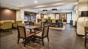 A spacious dining area with multiple tables and chairs, a television mounted on the wall, and a reception desk in the background. - Hampton Inn Dover (Dover)