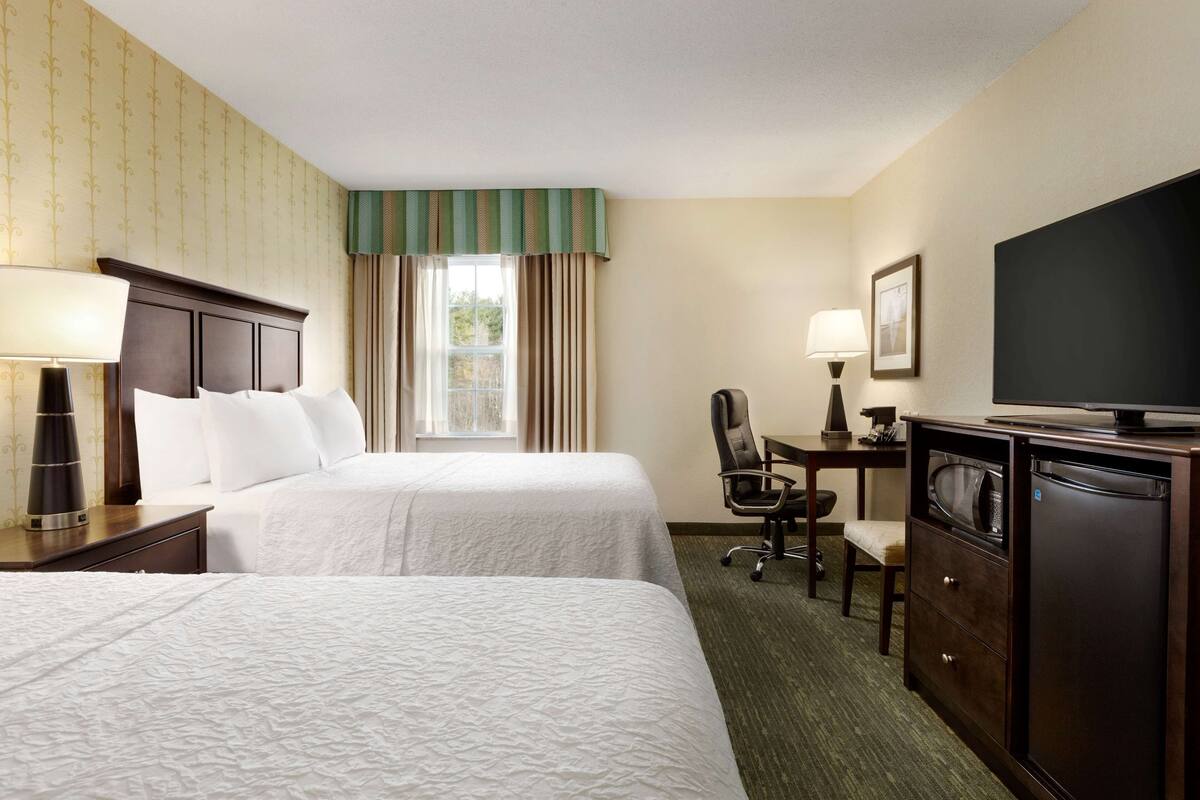 A hotel room with two beds, a desk with a chair, a television, and a minibar.