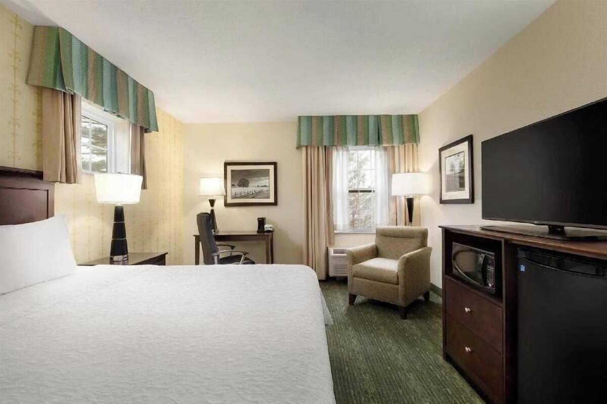A hotel room with a bed, desk, chair, television, and a microwave.