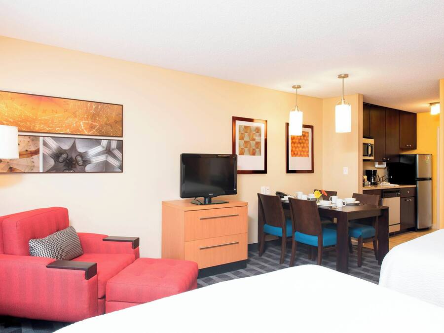 Ein Hotelzimmer mit einem roten Sofa, einem Fernseher auf einem Holzschrank, einem Esstisch mit Stühlen und einer Küchenzeile im Hintergrund.