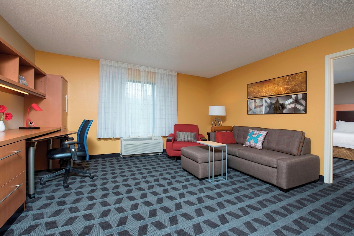 A hotel room with a desk, office chair, sofa, and a small table.