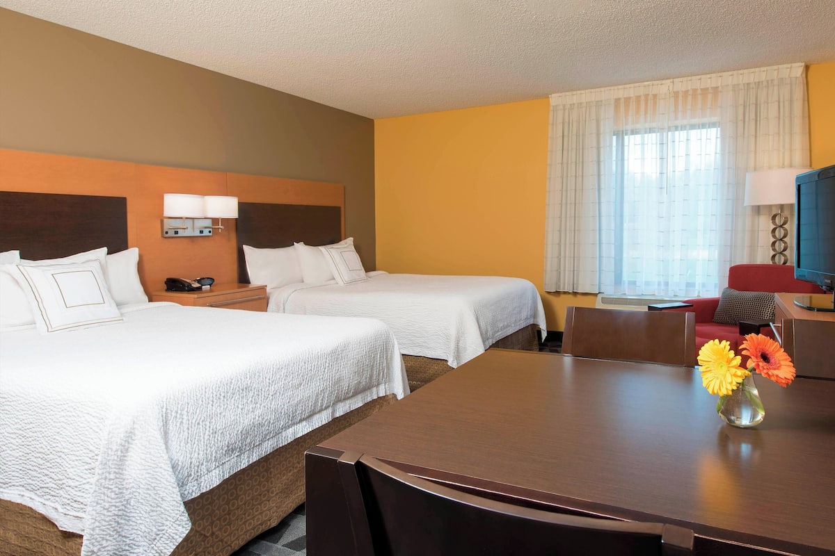 A hotel room with two beds, a desk, a chair, a TV, and a window with curtains.