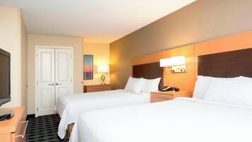 Two single beds with white linens, a flat-screen TV, and a nightstand with a lamp.
