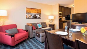 Quarto de hotel com área de jantar, sofá, televisão e cozinha.