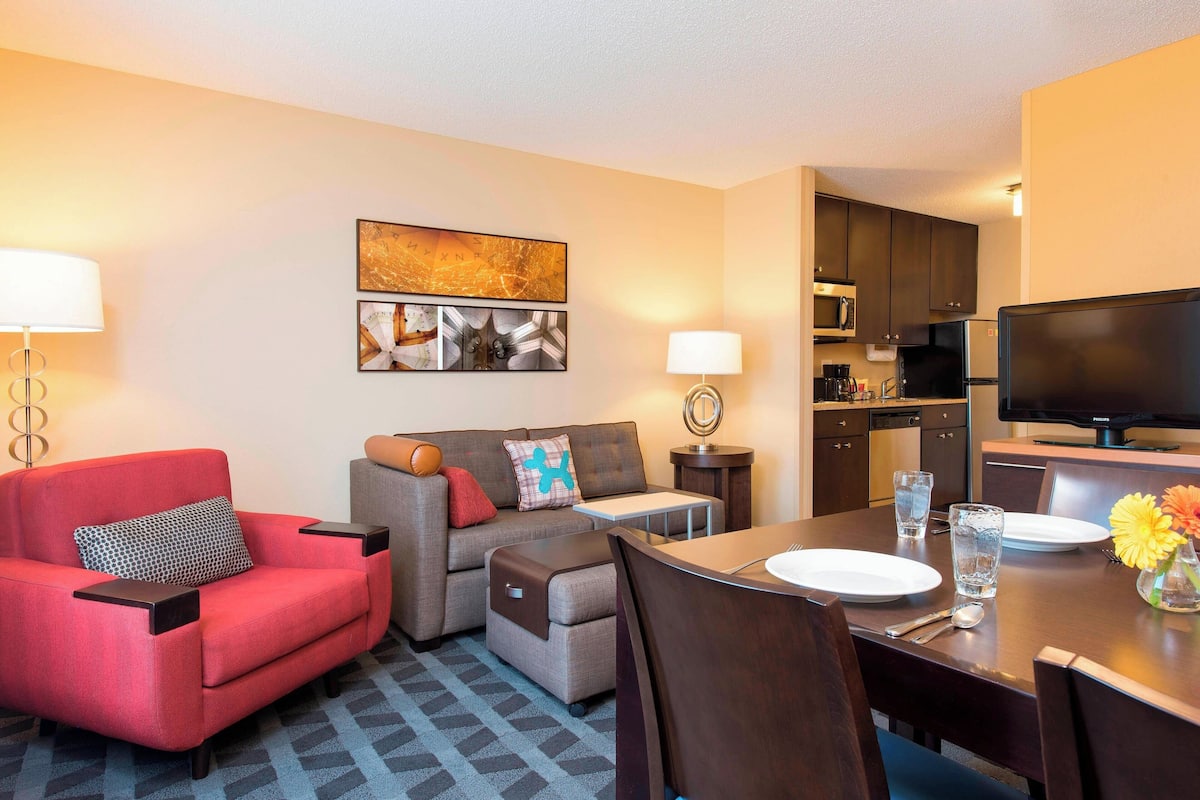 A hotel room with a dining area, a sofa, a TV, and a kitchen.