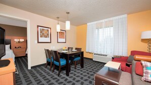Quarto de hotel com mesa de jantar, cadeiras, sofá, televisão e escrivaninha.