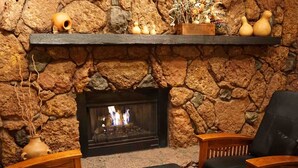 A stone fireplace with a fire, wooden chairs, and a shelf with decorative items. - Lodge At Sedona (Sedona)