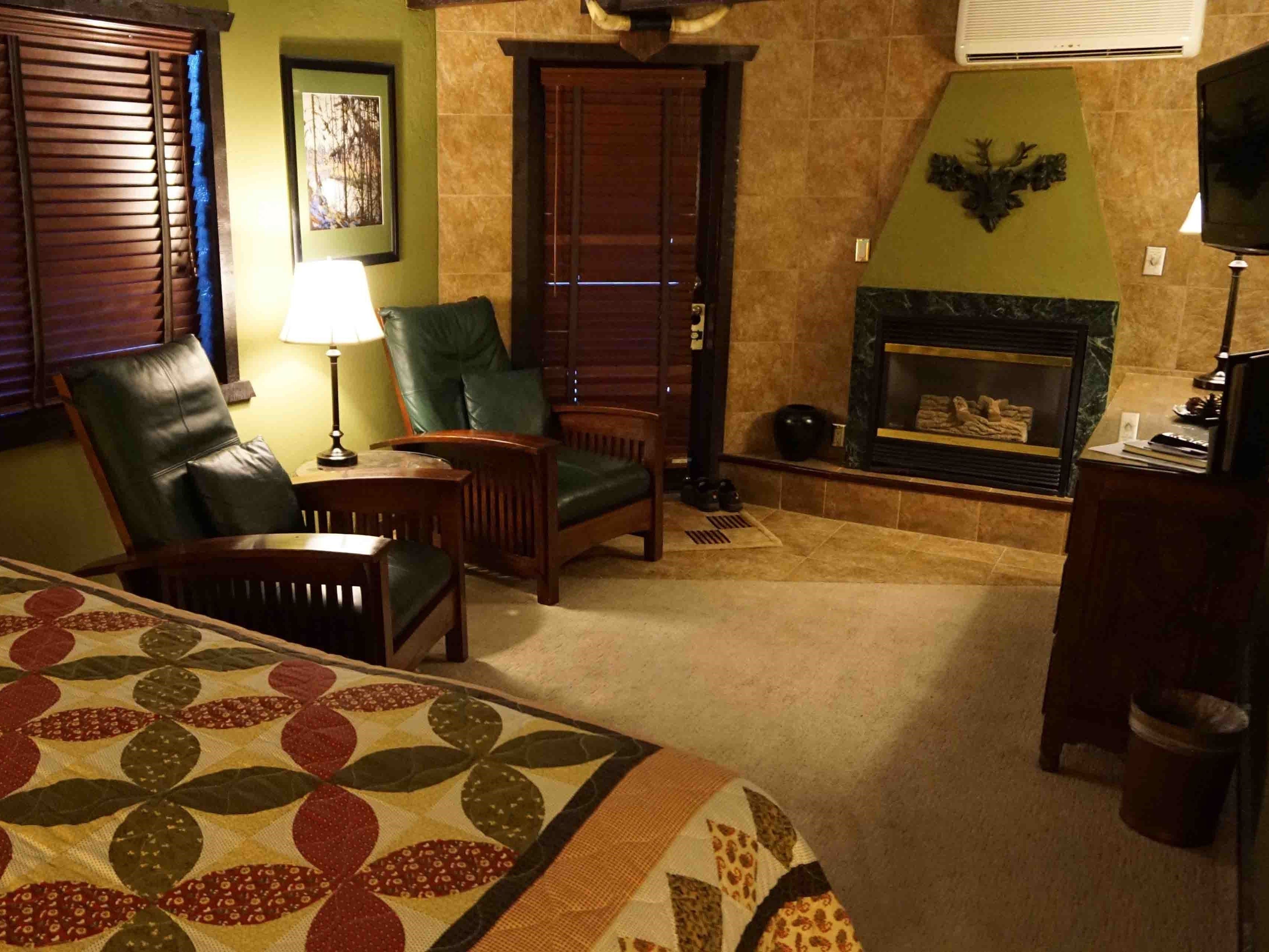 A cozy room with a fireplace, leather chairs, a bed with a floral bedspread, and a green accent wall.