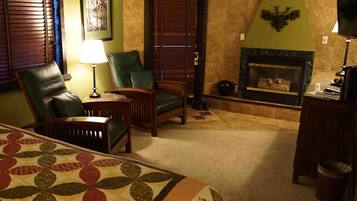 A cozy room with a fireplace, leather chairs, a bed with a floral bedspread, and a green accent wall.