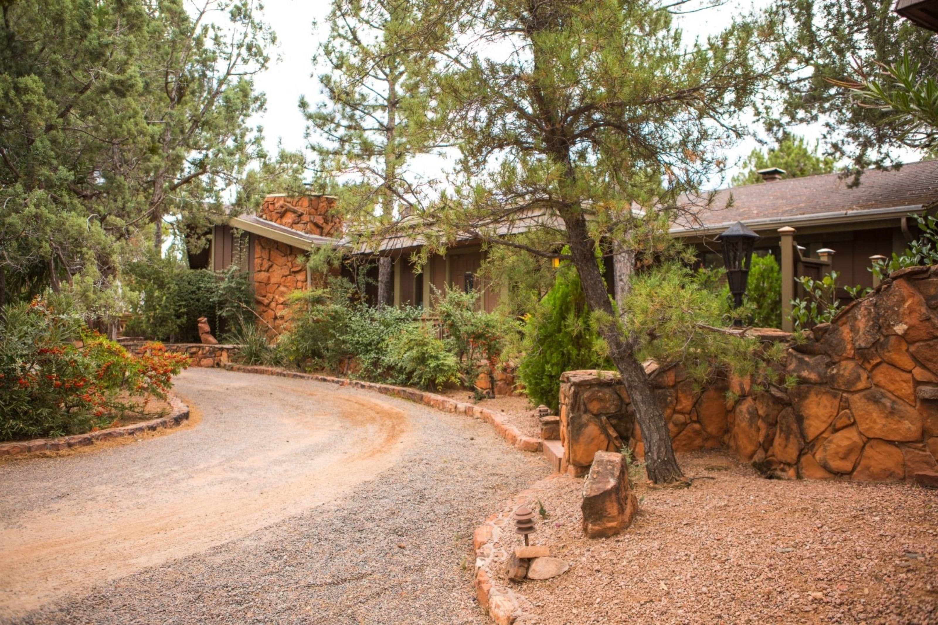 A rustic cabin with a stone exterior, surrounded by dense trees and a gravel driveway.