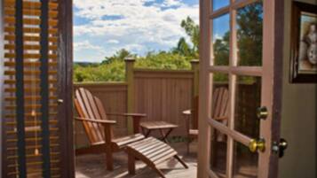 A wooden deck with two chairs and a table, a wooden fence, and a view of greenery.