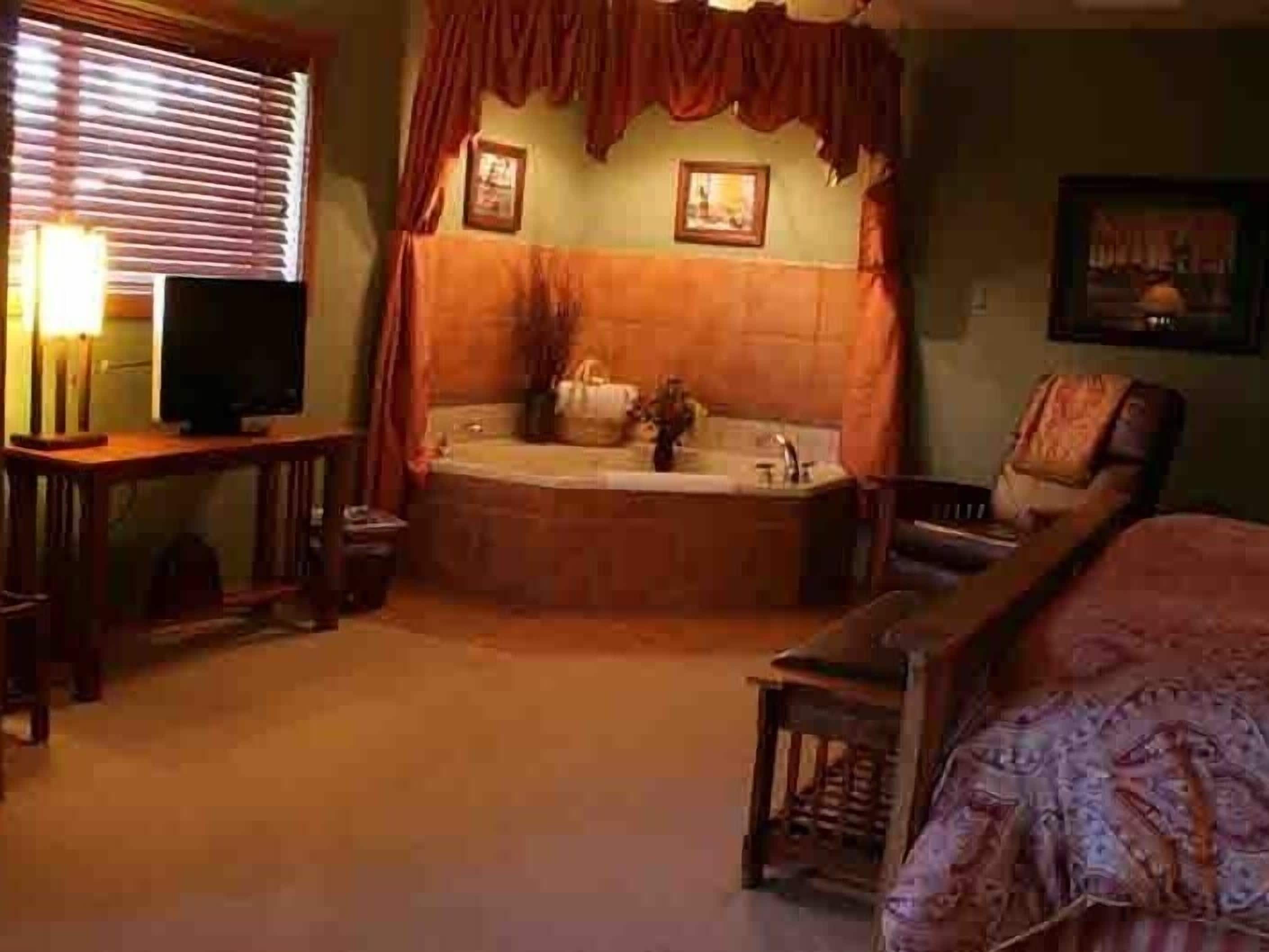 A room with a large bathtub, a wooden chair, a small table, and a television.