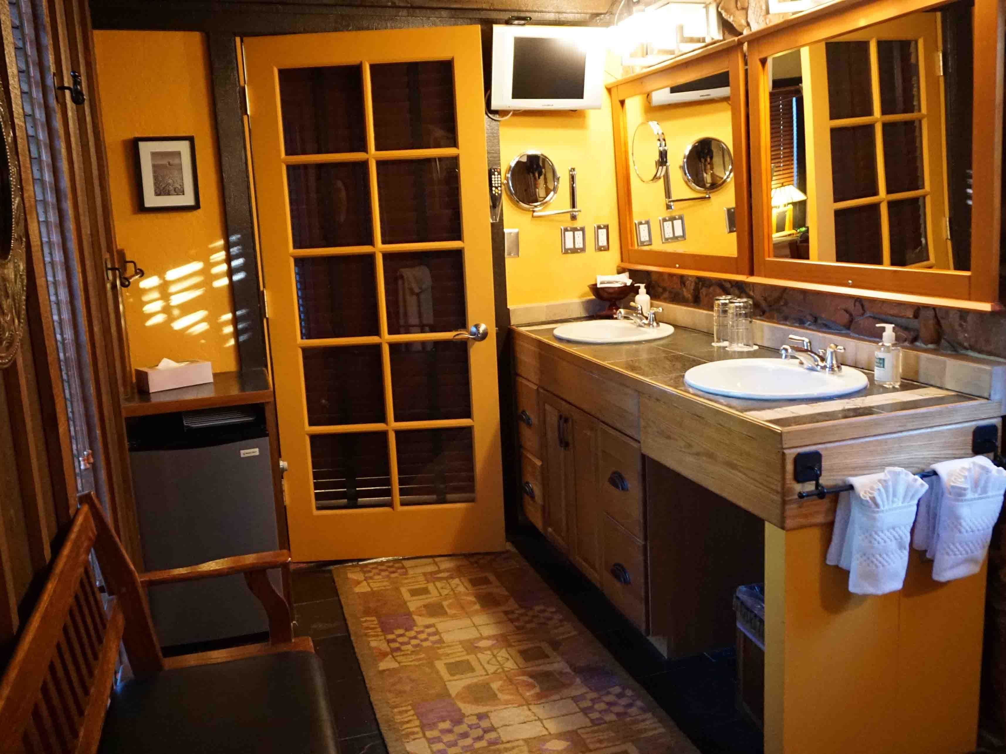 A bathroom with a wooden door, two sinks, a mirror, and a towel rack.