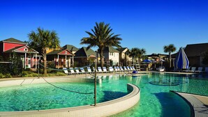 A large outdoor swimming pool with lounge chairs and palm trees, surrounded by houses. - Carriage House Hotel (Lafayette)