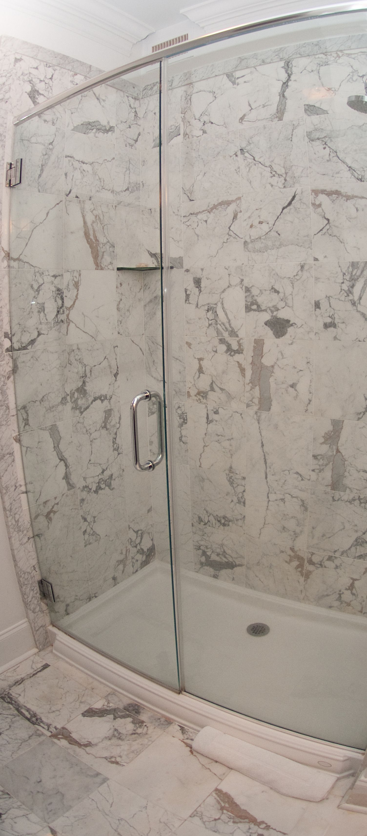 A glass-enclosed shower with a marble wall.