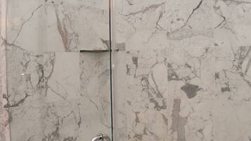 A glass-enclosed shower with a marble wall.