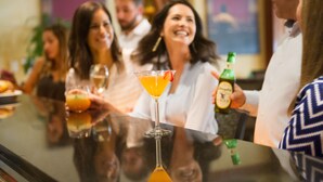 Un grup de persones a un bar, amb begudes i una ampolla de cervesa.