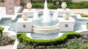 Una fontana envoltada per una paret de maó, palmeres i un jardí floral.